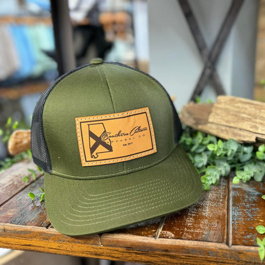 Green cap with leather patch on a wooden surface with plants