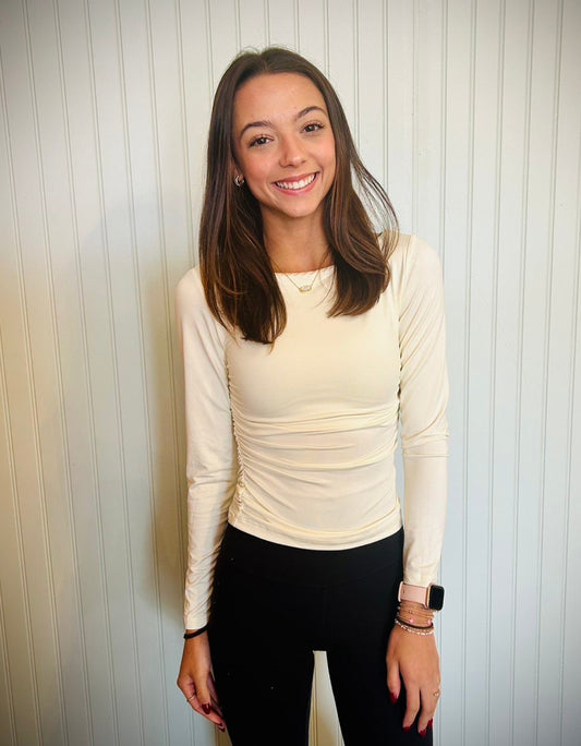 Woman wearing a cream long-sleeve top and black pants against a striped wall.