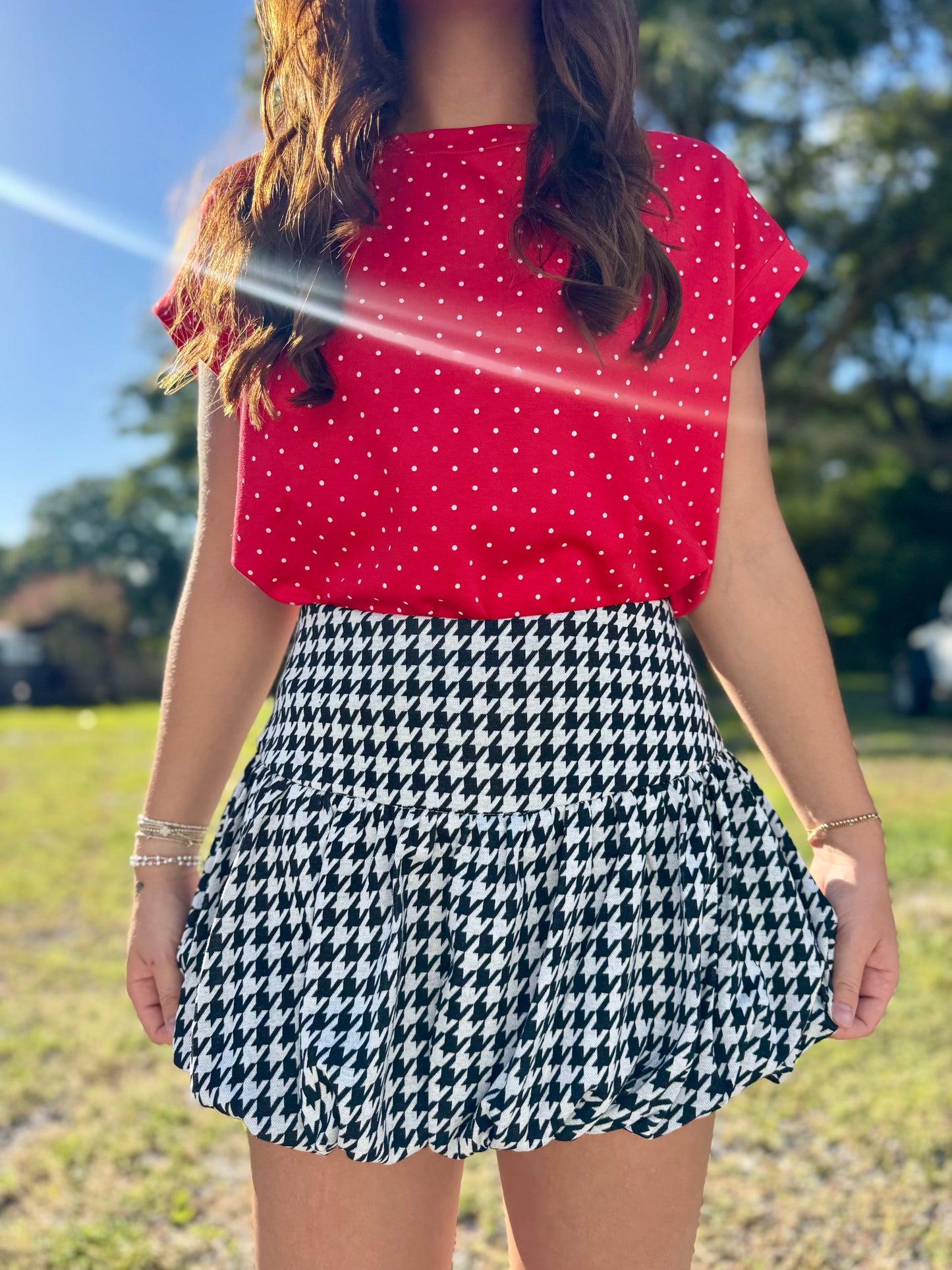 A woman outdoors wearing a bright red short-sleeve top with white polka dots and a black-and-white houndstooth skirt.